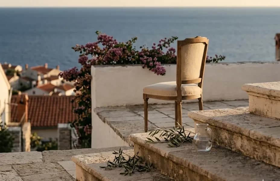 A linen chair on a stone terrace overlooking the Adriatic at golden hour